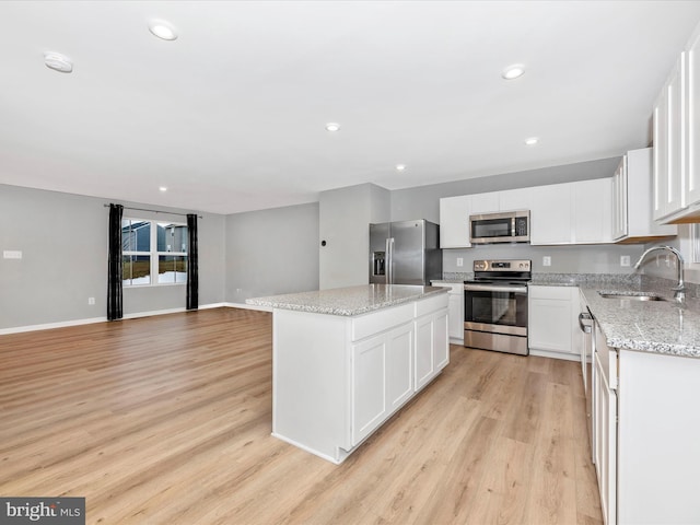 kitchen with a kitchen island, sink, stainless steel appliances, white cabinets, and light stone counters