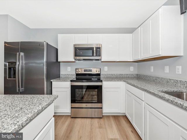 kitchen featuring light stone countertops, white cabinets, appliances with stainless steel finishes, light hardwood / wood-style floors, and sink