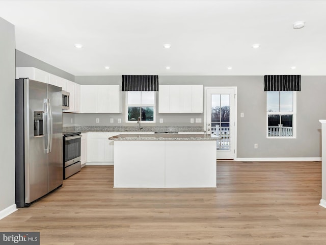 kitchen with light wood-type flooring, stainless steel appliances, white cabinetry, and a center island