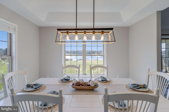 dining area featuring a chandelier, a raised ceiling, a water view, and a healthy amount of sunlight