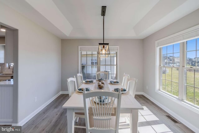 dining room with sink, a tray ceiling, and light wood-type flooring