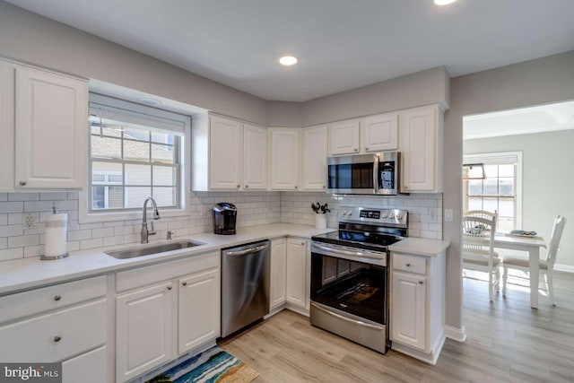 kitchen with light hardwood / wood-style floors, decorative backsplash, sink, white cabinetry, and appliances with stainless steel finishes