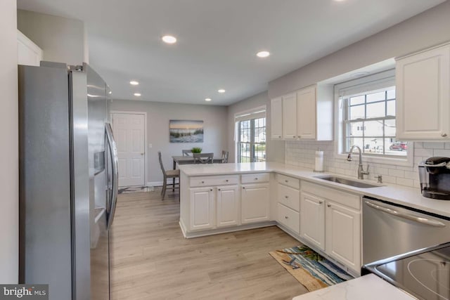 kitchen with kitchen peninsula, sink, stainless steel appliances, and white cabinetry