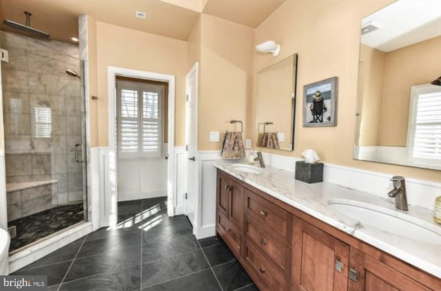 bathroom featuring double vanity, a stall shower, a sink, and wainscoting