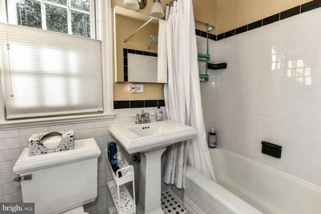 bathroom with toilet, a wainscoted wall, shower / bath combination with curtain, and tile walls