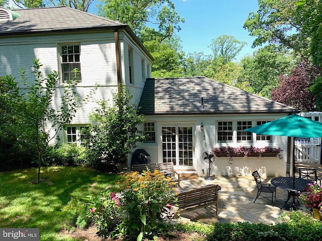 back of property with entry steps, a patio, roof with shingles, a yard, and brick siding