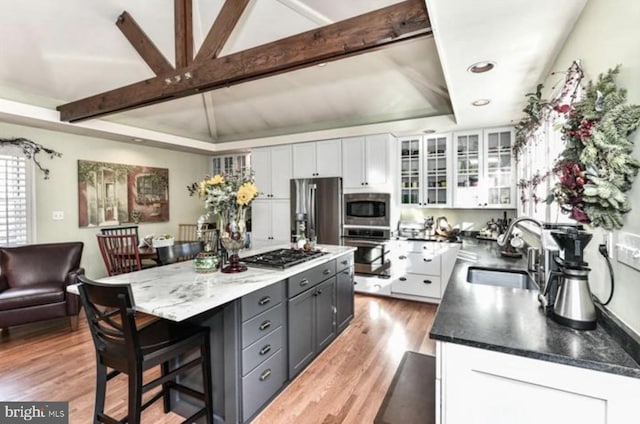 kitchen featuring a breakfast bar, appliances with stainless steel finishes, white cabinets, a sink, and light wood-type flooring