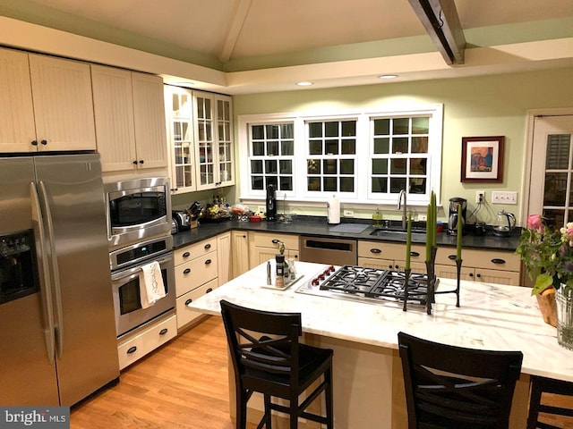 kitchen with a breakfast bar, lofted ceiling, appliances with stainless steel finishes, a sink, and light wood-type flooring