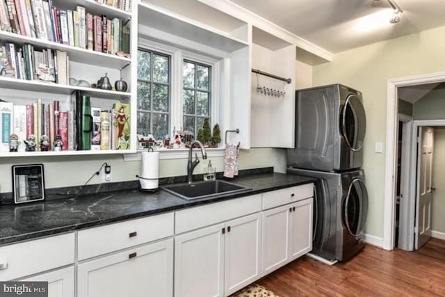 laundry room with stacked washer and clothes dryer, dark wood finished floors, cabinet space, a sink, and track lighting