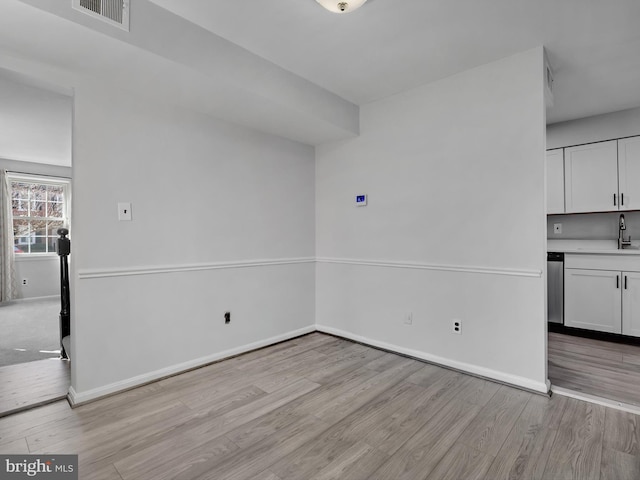 unfurnished dining area featuring light wood-style floors, baseboards, visible vents, and a sink