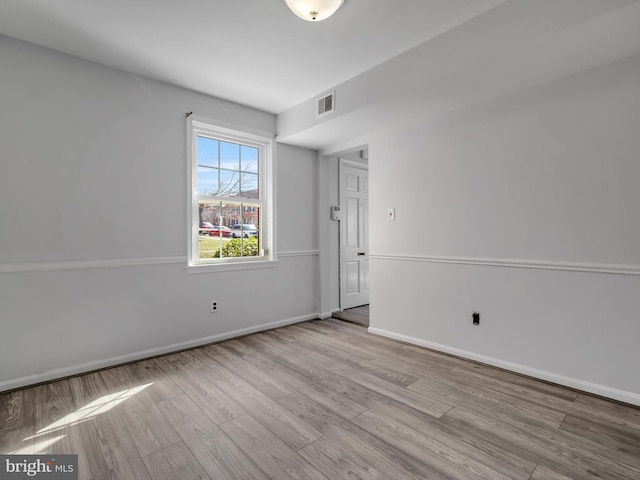 spare room with wood finished floors, visible vents, and baseboards