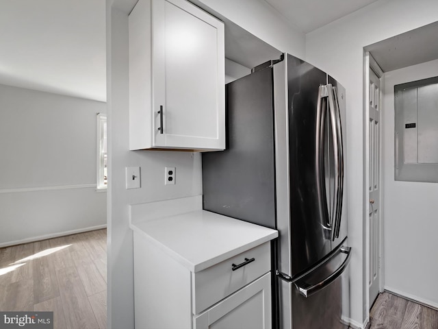 kitchen with white cabinetry, light countertops, freestanding refrigerator, electric panel, and light wood finished floors