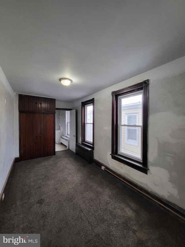 unfurnished room featuring baseboard heating and dark colored carpet