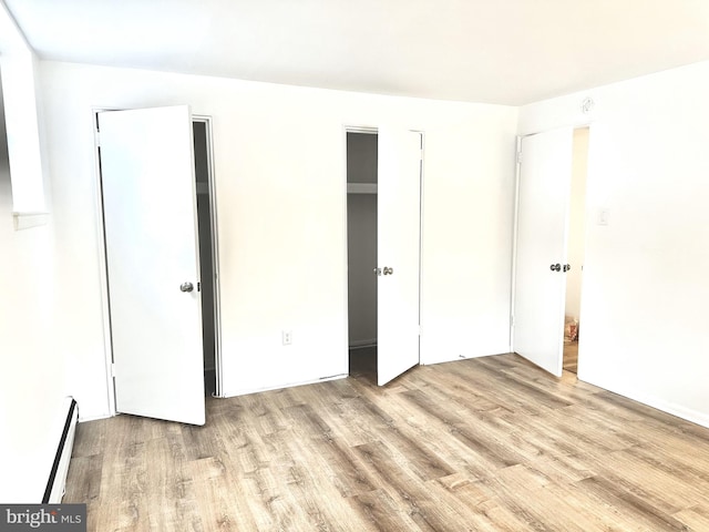 unfurnished bedroom with light wood-type flooring and a baseboard heating unit