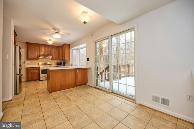 kitchen featuring stainless steel appliances, decorative backsplash, kitchen peninsula, ceiling fan, and light tile patterned floors