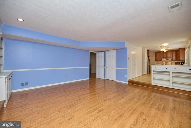 unfurnished living room with light wood-type flooring, a textured ceiling, and ceiling fan