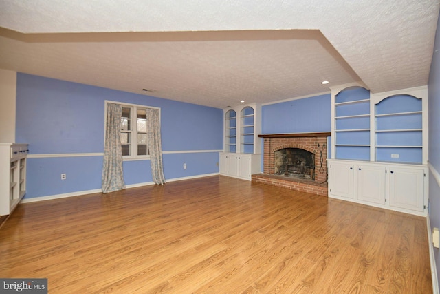 unfurnished living room with a fireplace, a textured ceiling, light wood-type flooring, built in shelves, and lofted ceiling