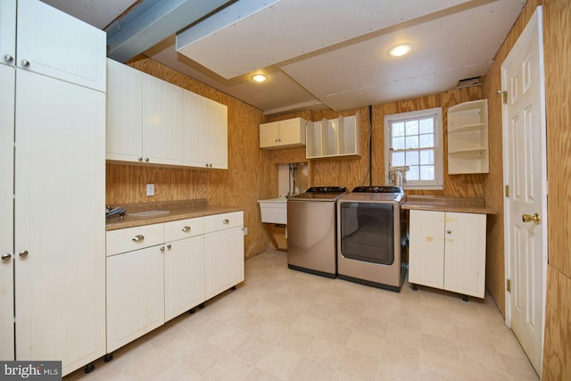 washroom featuring sink, washer and clothes dryer, wood walls, and cabinets