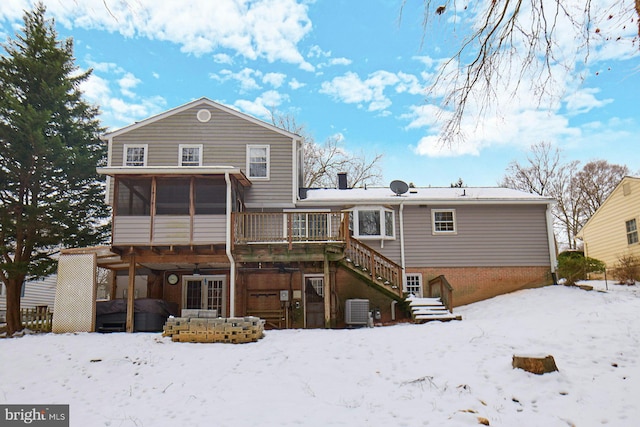 snow covered back of property featuring central AC unit, a sunroom, and a hot tub