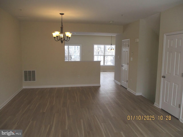 empty room with dark hardwood / wood-style flooring and an inviting chandelier