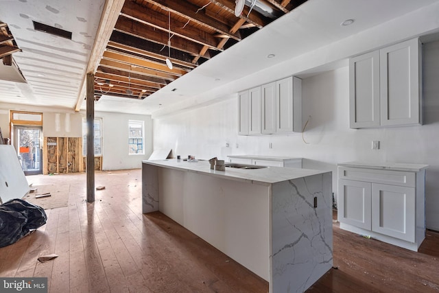 kitchen with hardwood / wood-style floors, light stone countertops, white cabinets, and a center island with sink