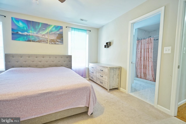 bedroom with ceiling fan, light colored carpet, and ensuite bath