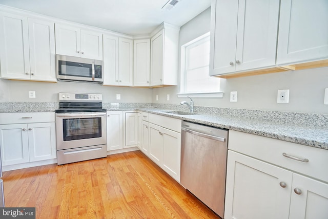 kitchen with white cabinetry, light hardwood / wood-style floors, stainless steel appliances, light stone countertops, and sink