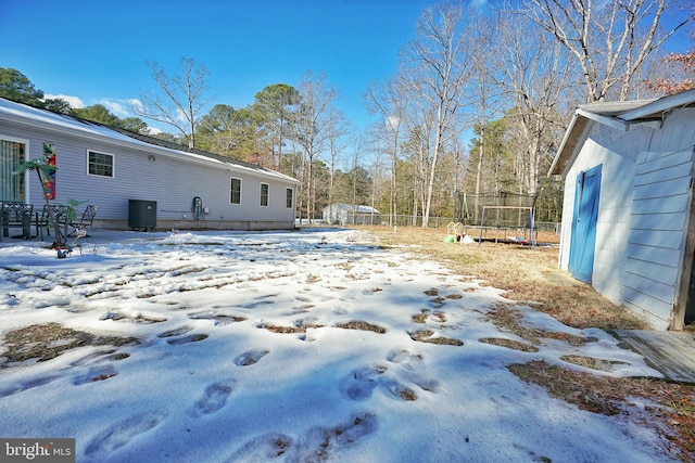 snowy yard featuring central AC and a trampoline