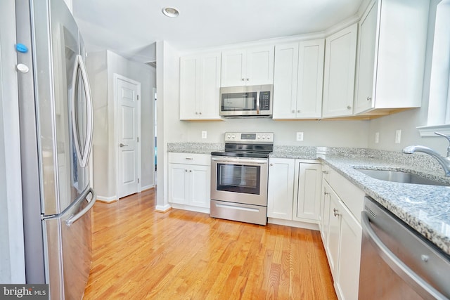 kitchen featuring appliances with stainless steel finishes, light wood-type flooring, white cabinets, light stone counters, and sink