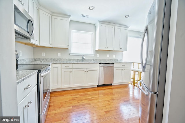 kitchen with light hardwood / wood-style floors, stainless steel appliances, white cabinets, light stone counters, and sink