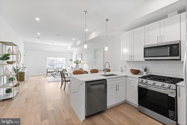 kitchen featuring stainless steel appliances, decorative backsplash, hanging light fixtures, white cabinets, and sink