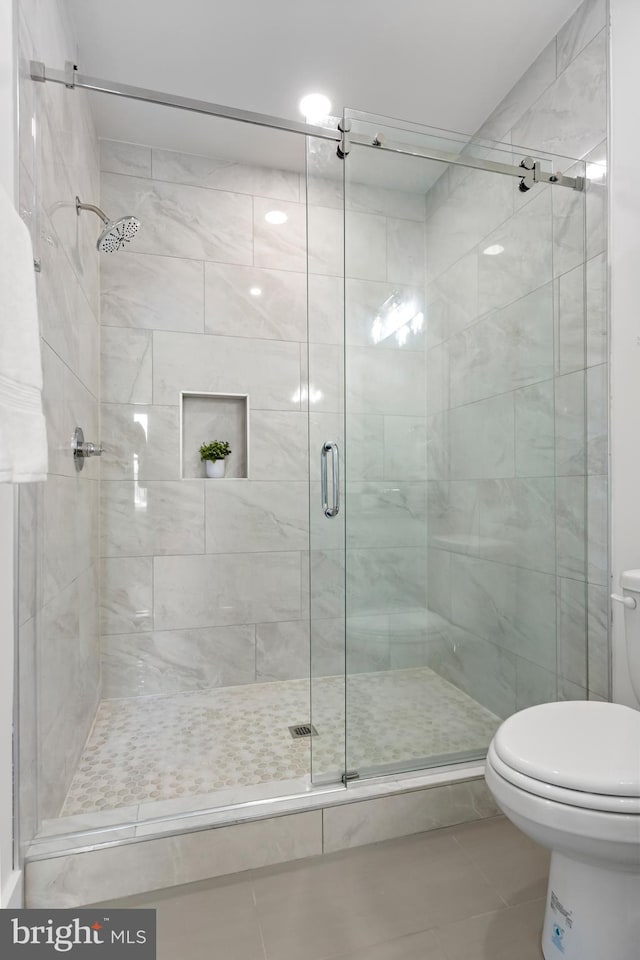 bathroom featuring toilet, tile patterned flooring, and a shower with shower door