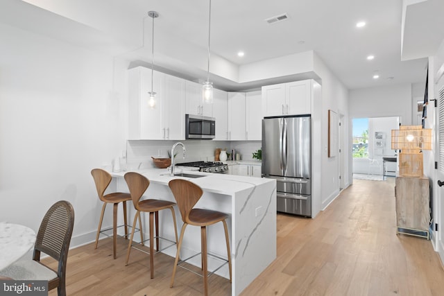 kitchen with decorative light fixtures, backsplash, kitchen peninsula, white cabinetry, and appliances with stainless steel finishes