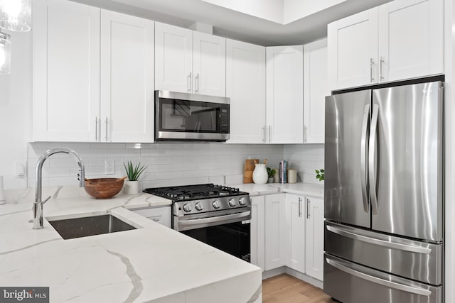 kitchen featuring light stone countertops, white cabinetry, stainless steel appliances, decorative backsplash, and sink