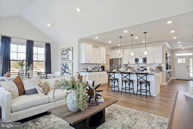 living room with vaulted ceiling, ornamental molding, and light wood-type flooring