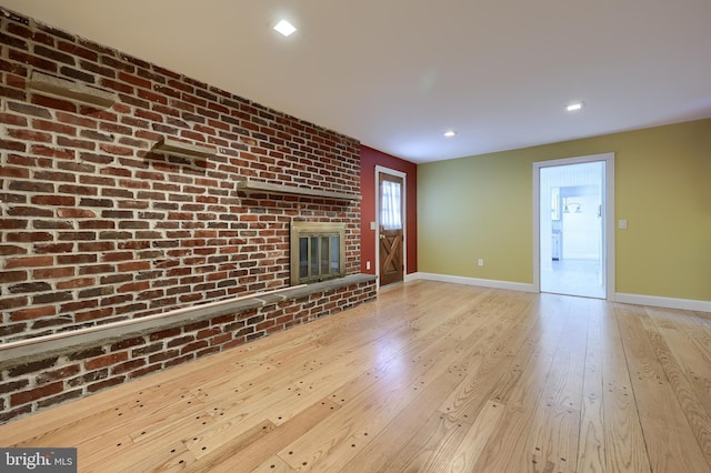 unfurnished living room featuring a brick fireplace, brick wall, and light wood-type flooring