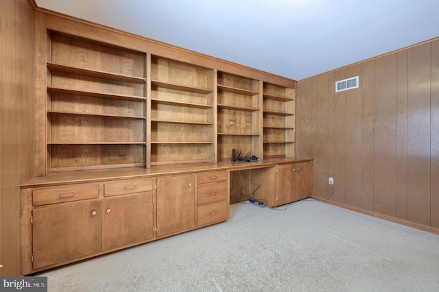 unfurnished office featuring built in desk, light colored carpet, and wooden walls