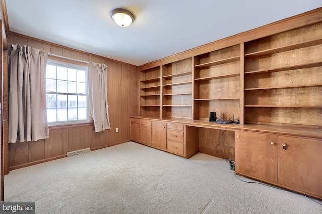 unfurnished office featuring built in desk, light carpet, and wood walls