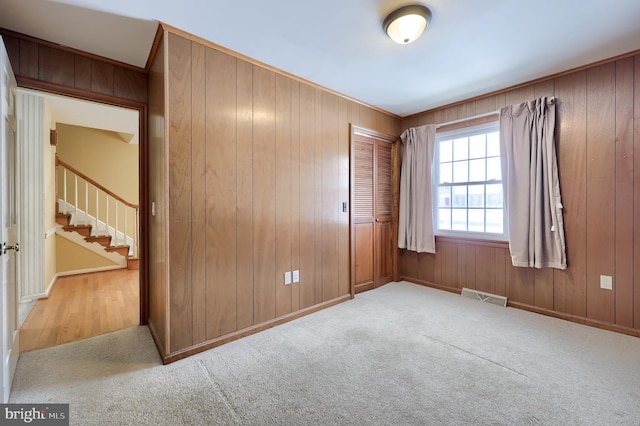 unfurnished bedroom featuring light carpet, wood walls, and a closet