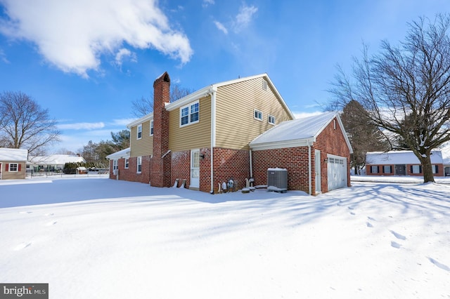 snow covered back of property featuring a garage and central air condition unit