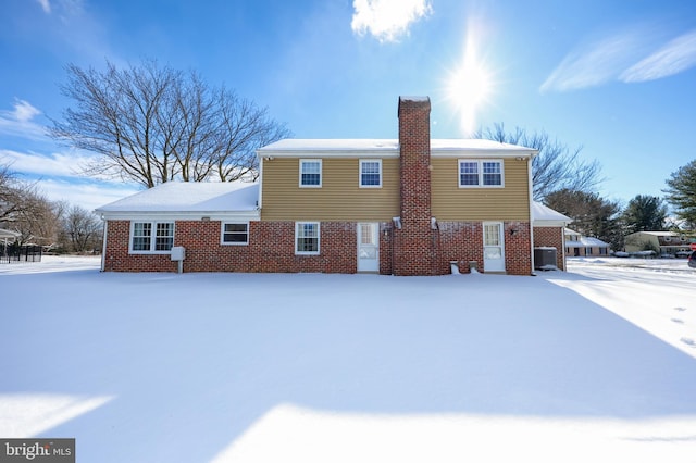 snow covered rear of property featuring central AC