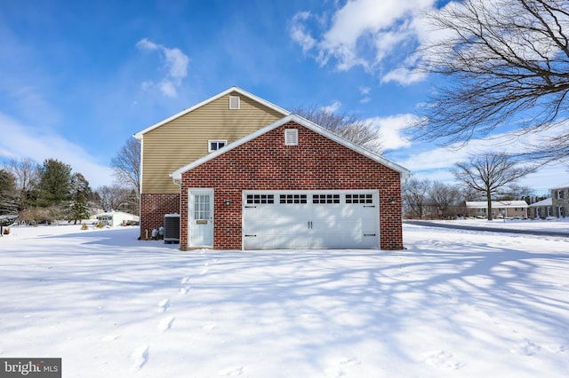 snow covered property featuring a garage and central air condition unit