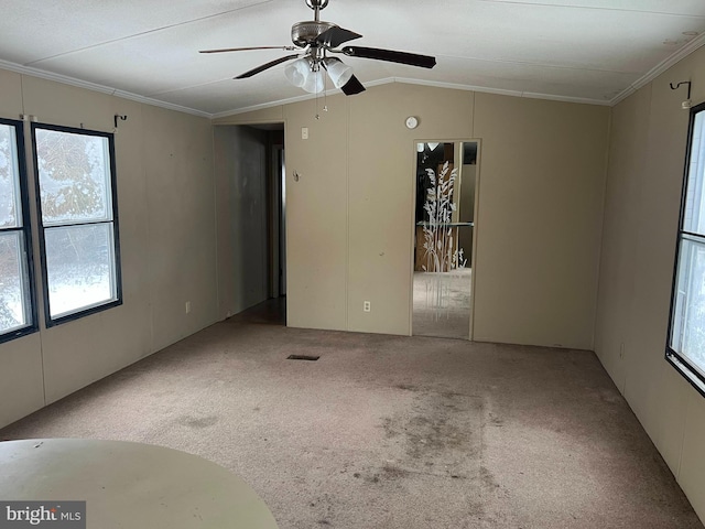 carpeted spare room featuring ceiling fan, crown molding, vaulted ceiling, and a healthy amount of sunlight