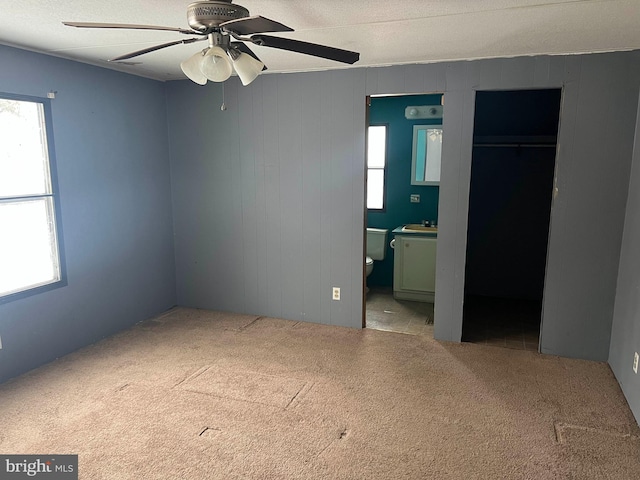 unfurnished bedroom with ensuite bath, wooden walls, light colored carpet, and ceiling fan