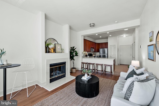 living area featuring a premium fireplace, baseboards, dark wood-style flooring, and recessed lighting