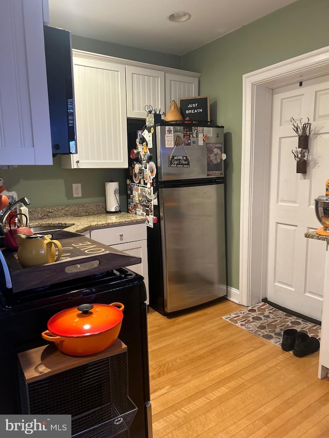 kitchen featuring sink, light hardwood / wood-style flooring, stainless steel fridge, black range with electric stovetop, and white cabinets