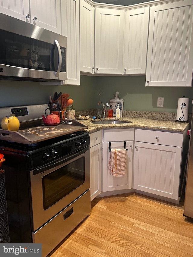 kitchen featuring sink, stainless steel appliances, light stone countertops, light hardwood / wood-style floors, and white cabinets