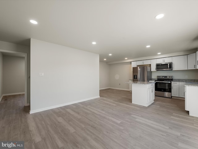 kitchen featuring light wood-type flooring, stainless steel appliances, a kitchen island, light stone counters, and white cabinets