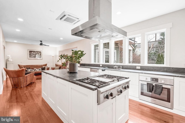 kitchen with stainless steel appliances, island exhaust hood, white cabinets, and light hardwood / wood-style floors