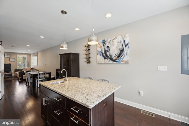 kitchen with decorative light fixtures, a center island with sink, sink, light stone countertops, and dark hardwood / wood-style flooring